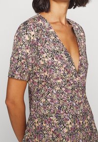 Robe fleurie en tissu léger, avec un décolleté en V et des manches courtes. Le motif comprend des fleurs roses, vertes et violettes sur un fond sombre.