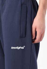 Tengerészkék szabadidőnadrág puha anyagból, oldalzsebbel és fehér hímzett "lowlights" logóval az alsó lábszáron.