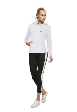 Fehér kapucnis pulóver kék és sárga békejellel, fekete leggings-el, fehér oldalsávokkal és fehér sportcipővel párosítva.
