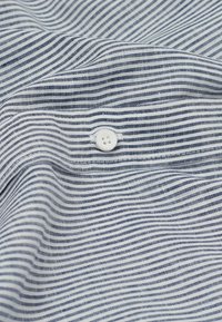 Baumwollstoff mit navyblauen und weißen vertikalen Streifen. Verfügt über einen auf den Stoff genähten weißen Knopf, der Textur und Details hinzufügt.
