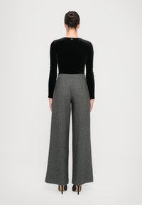 Čierny zamatový top s dlhým rukávom spárovaný so šedými širokými nohavicami s vzorom houndstooth a vysokým pásom, končiacimi v strede lýtok.