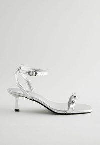 Silver metallic high-heel sandal with a square toe, thin ankle strap, and a glossy finish. Features a slender heel and subtle buckle detail.