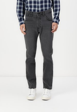 Donkergrijze denim jeans met een rechte pijp, vijf zakken en zichtbare stiksels, gecombineerd met witte sneakers en een blauw geruit shirt.