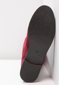 Botte en daim bordeaux avec semelle en caoutchouc noir texturé ; indique la taille 37. Vue centrée sur la semelle et le détail latéral.