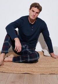 Top de manga larga navy con cuello abotonado y pantalones de pijama con estampado de cuadro en navy, rojo y blanco. Textura de punto liso, corte casual.