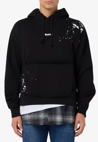 Felpa nera con tasca frontale e design a macchie di vernice bianca sul lato destro. Dotata di cappuccio con coulisse e tessuto morbido.