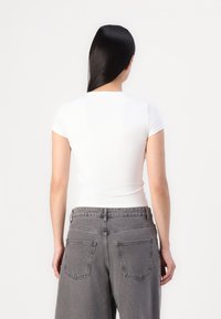Hvit tettsittende t-skjorte med korte ermer, kombinert med høytidelte grå denimjeans med to baklommer og en falmet tekstur.