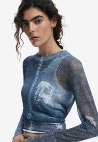 Long-sleeve top in a blue denim print with a textured knit; features a rounded neckline and fitted silhouette.