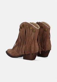 Botines de ante marrón con flecos, botones decorativos de latón, puntera ligeramente curvada y tacones de madera. Cierre de cremallera lateral para facilitar su uso.
