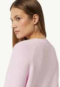 Light pink ribbed knit sweater with a round neckline, featuring a textured finish and dropped shoulder design.