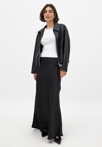 Schwarze Lederjacke, weißes enges T-Shirt und ein langer schwarzer Rock. Das Outfit zeichnet sich durch glatte Texturen und ein elegantes, minimalistisches Design aus.