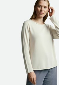 Hellbeiges Langarmshirt mit rundem Ausschnitt und feiner Struktur, kombiniert mit schimmernden grauen Hosen.