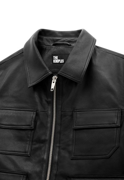 Black leather jacket with silver front zipper, two flap pockets on chest, and wide collar, branded "THE KOOPLES" inside collar.