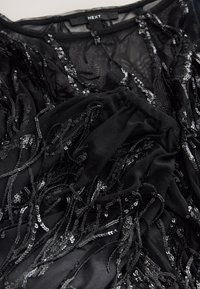 Haut en maille noire avec des paillettes noires tombantes et des couches texturées. Le design comprend des détails à franges complexes et un col rond.