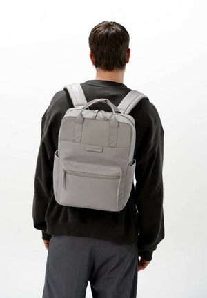 Grauer Stoff-Rucksack mit gepolsterten Tragegurten und einem Handgriff oben; verfügt über eine Vordertasche mit Reißverschluss und Seitentaschen. Minimalistisches Design.