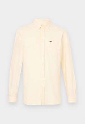 Chemise crème à manches longues avec col et poche poitrine, ornée d'un logo crocodile vert brodé.