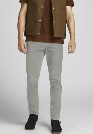 Pantaloni di cotone grigi con vestibilità slim, abbinati a un gilet marrone e scarpe nere. I pantaloni hanno una texture liscia e un design minimalista.