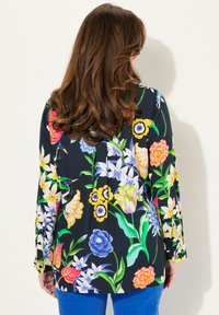 Halenka s dlouhým rukávem na černém pozadí se živým květinovým vzorem v různých barvách, vyrobená z lehkého materiálu, volný střih.