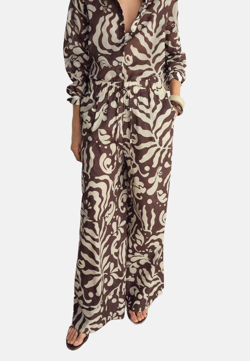 Brun og beige mønstret jumpsuit med lange ærmer, krave, elastisk talje og vid ben-design, der har abstrakte blomstermotiver.
