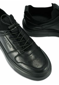Para czarnych skórzanych sneakersów z elastycznymi sznurowadłami, perforowaną strefą palców i wytłoczonym logiem marki na boku.