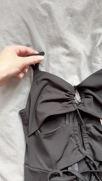 Čierny odev so zhrnutou prednou časťou, nastaviteľnými ramienkami a uzatváraním na zips. Má vrecká a textúrovanú látku. Hladký a elegantný vzhľad.