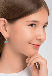 Zilveren visvormige oorbellen met turquoise accenten, met een glanzend, gestructureerd ontwerp, gedragen door een model tegen een neutrale achtergrond.