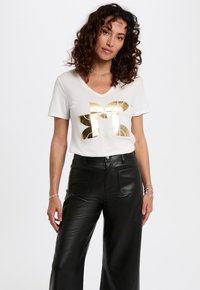 Witte v-hals t-shirt met een grote gouden metallic vlinderafbeelding. Gepaarde met hoge zwarte faux-leer wijde broek.