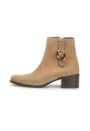 Beige ruskind ankle støvle med lav blokhæl og gulddetaljeret spænde på ydersiden mod hvid baggrund.