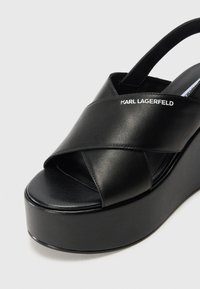 Sandali platform neri con design a strappo incrociato, realizzati in pelle liscia. Presentano una suola spessa e solida e un logo impresso sulla fascia.