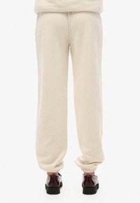 Pantaloni sportivi beige in cotone con vestibilità rilassata, con polsini elasticizzati alle caviglie e una cintura con cordino, abbinati a scarpe nere.