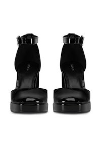 Zapatos de tacón plataforma de charol negro con correas en los tobillos, que cuentan con una textura suave y un diseño de punta redondeada.