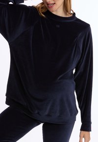 Navy velours lange mouw top met een ronde halslijn en een losse pasvorm. Beschikt over een zachte textuur en subtiele logodetail op de borst.