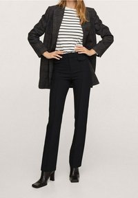Blazer à carreaux noirs sur une chemise rayée blanche et noire, associé à un pantalon noir taille haute et des bottines à talons noires.