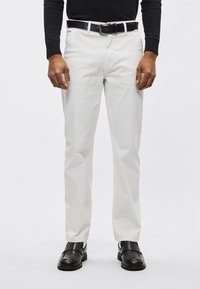 Białe bawełniane spodnie o prostym kroju, z bocznymi kieszeniami i czarnym skórzanym paskiem. Czarna loafers dodają kontrastu.