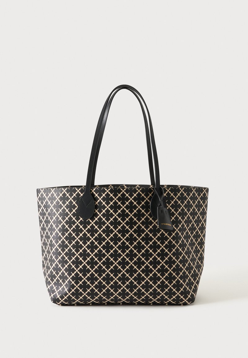 Sac fourre-tout noir avec motif croisé beige, deux longues poignées et une étiquette suspendue sur un fond clair uni.