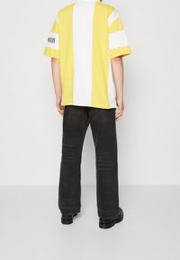 Short-sleeve, yellow and white striped t-shirt with a relaxed fit, paired with black, straight-leg pants and black footwear.