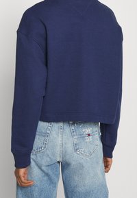 Marinblå kort tröja i mjukt tyg, med rund halsringning och sänkta axlar. Bärs tillsammans med ljusblå jeans i denim som har logotypdetaljer.