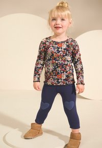 Blumenmuster Langarmoberteil in Marineblau mit bunten Blumen. Marinefarbene Leggings mit herzförmigen Akzenten an den Knien. Tan Suede Knöchelschäfte.