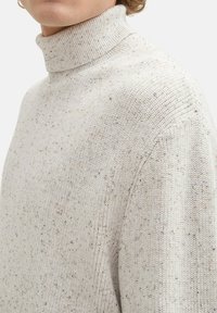Hellgrauer Strickpullover mit Rollkragen, der eine strukturierte Oberfläche mit gesprenkelten Akzenten in dunkleren Farbtönen aufweist. Enganliegendes Design, gerippter Kragen.