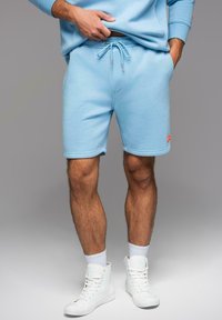 Šortky z bavlny v nebesky modré barvě s elastickým pasem, šňůrkou na stažení a předními kapsami. Na levém lemu se nachází malé červené logo.