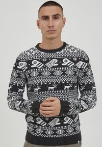 Gestrickter Pullover in Schwarz und Weiß mit einem Muster aus Schneeflocken, Rentieren und geometrischen Formen. Gerippter Halsausschnitt und Bündchen.