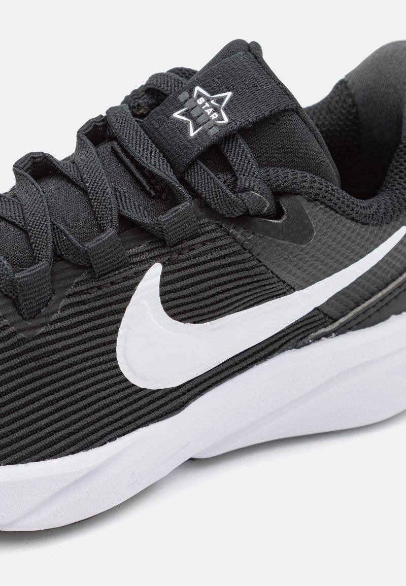 Scarpa sportiva nera con tomaia in tessuto testurizzato, caratterizzata da un'importante logo Swoosh bianco di Nike e lacci neri. Suola in gomma visibile sul fondo.