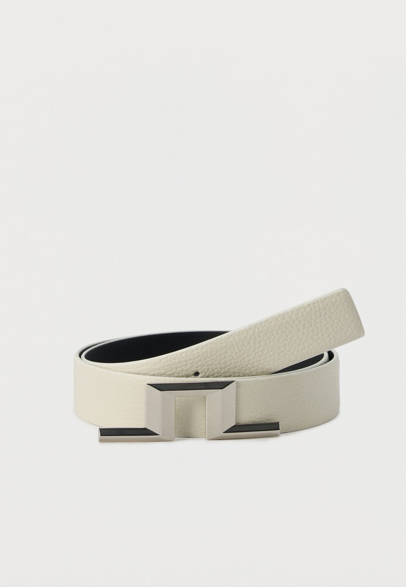 Δερμάτινη ζώνη σε ανοιχτό μπεζ με υφή, με ασημένια γεωμετρική μεταλλική αγκράφα, τυλιγμένη σε λευκό φόντο.