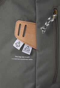 Graue Stofftasche mit strukturierten Oberflächen, ausgestattet mit einem Lederakzent, zwei Etiketten und einem Text, der angibt, dass sie aus recycelten Wasserflaschen hergestellt ist.