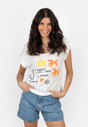 Woman smiling with long dark hair wearing white t-shirt with sun, palm trees, shell, and text "Sole, Mare e Amore" and denim shorts.