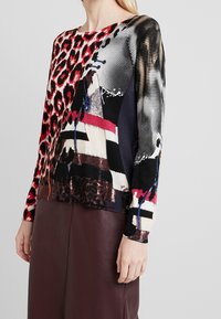 Pull à manches longues avec motifs mélangés, comprenant un imprimé léopard rouge et noir, des motifs géométriques, et un col rond. Finition en tissu doux.