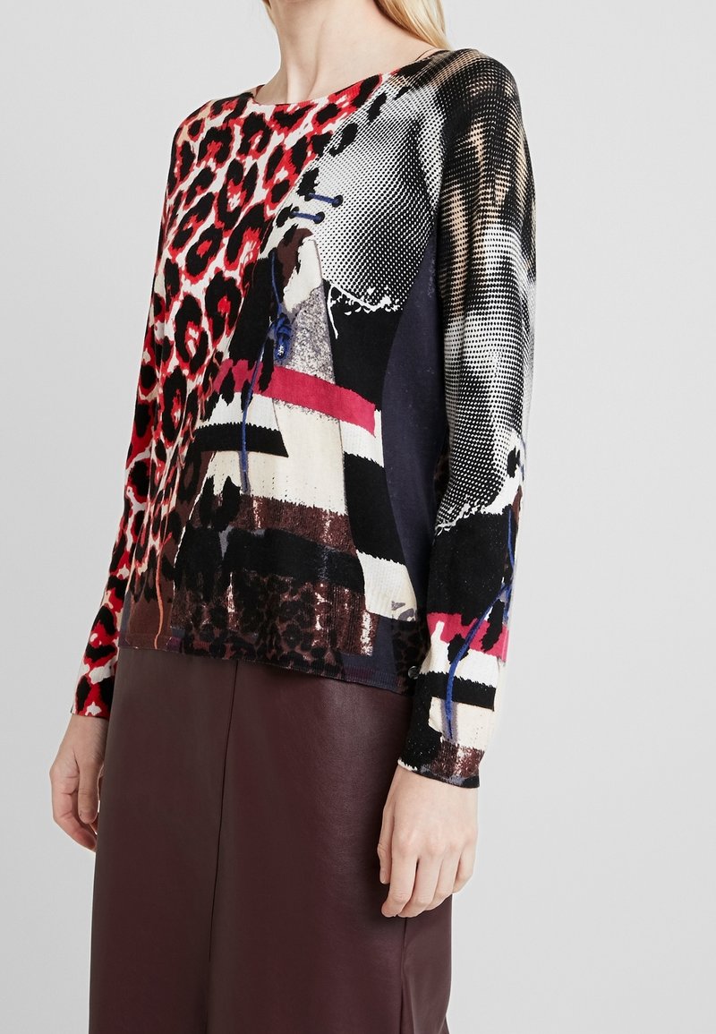 Pull à manches longues avec motifs mélangés, comprenant un imprimé léopard rouge et noir, des motifs géométriques, et un col rond. Finition en tissu doux.