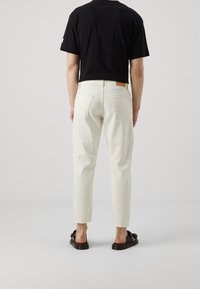 Bílé zkrácené kalhoty z denimu s přiléhavým pasem, dvěma zadními kapsami a hnědou koženou cedulkou na zadním pásku.