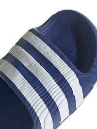 Modri gumijasti natikač z tremi belimi črtami, ki ima teksturiran vzorec na zgornjem delu za boljši oprijem. Odprt sprednji del.