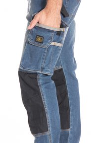 Un pantalon en jean avec des accents en tissu noir, plusieurs poches, des coutures visibles et une étiquette avec logo à l'arrière. Le design présente une coupe ajustée.